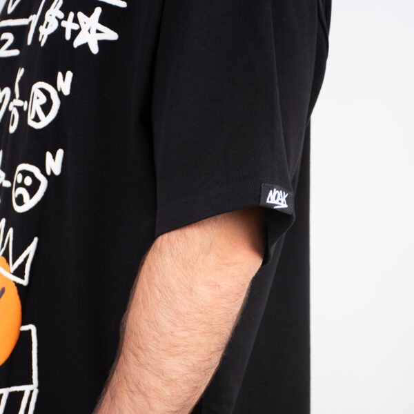 Detalle de manga de camiseta negra con etiqueta 'NOAK' en el dobladillo y diseño gráfico blanco.
