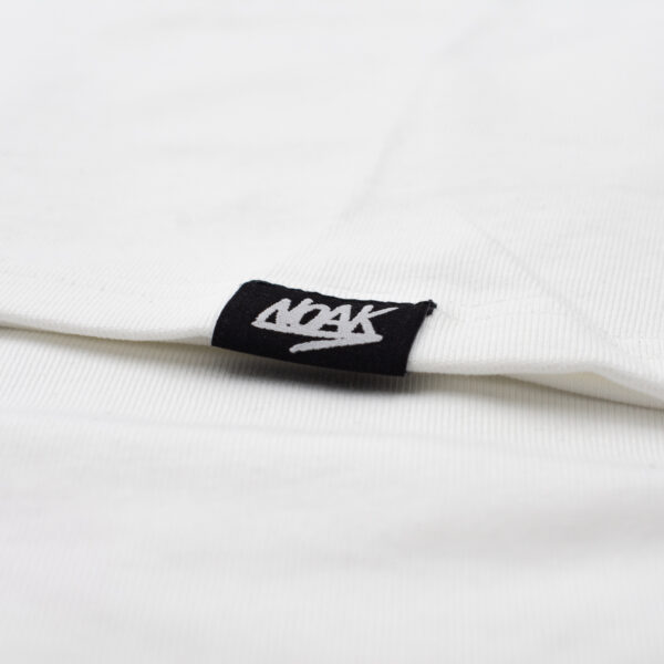 Detalle del dobladillo de una prenda blanca con etiqueta negra y el logo 'NOAK' en blanco.