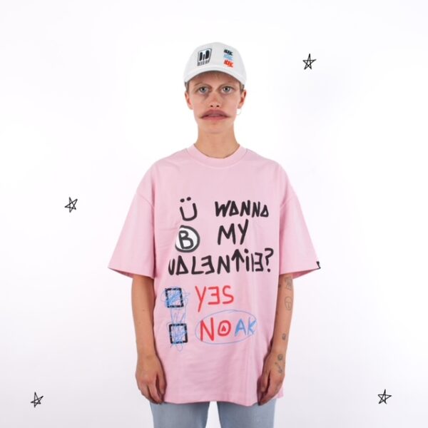 Persona con camiseta rosa de texto negro y rojo que dice 'Ü WANNA B MY VALENTINE?', con opción 'YES' o 'NOAK'