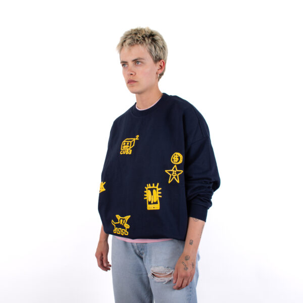 Sudadera azul marino con bordados amarillos de símbolos geométricos y figuras abstractas, usada por una persona con jeans.