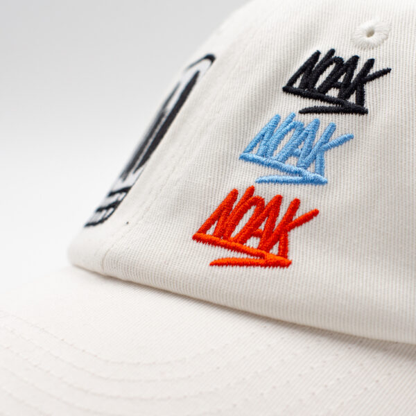 Detalle de bordado negro en gorra blanca con diseño de calavera rectangular y dientes cuadrados.
