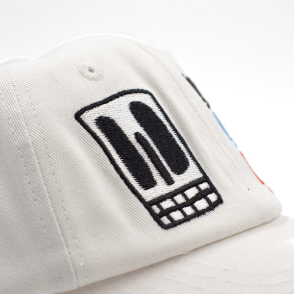 Detalle de bordado negro en gorra blanca con diseño de calavera rectangular y dientes cuadrados.