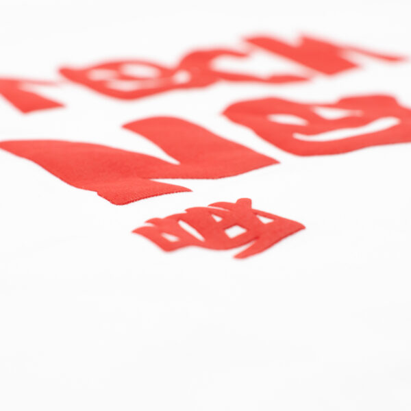 Detalle de estampado en relieve rojo sobre tela blanca con letras irregulares y caritas sonrientes.