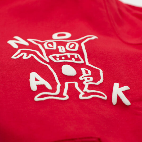Detalle de bordado en alto relieve de una figura abstracta con la palabra 'NOAK' en blanco sobre tela roja.