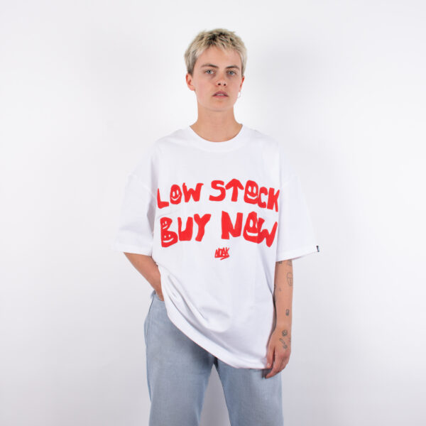 Persona con camiseta blanca de texto rojo 'LOW STOCK BUY NOW', con un diseño de tipografía irregular.