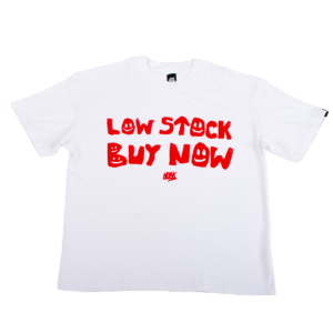 Camiseta blanca con la frase 'LOW STOCK BUY NOW' en rojo, con tipografía irregular y detalles de caritas sonrientes.