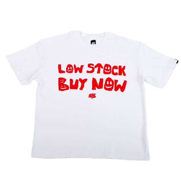 Camiseta blanca con la frase 'LOW STOCK BUY NOW' en rojo, con tipografía irregular y detalles de caritas sonrientes.